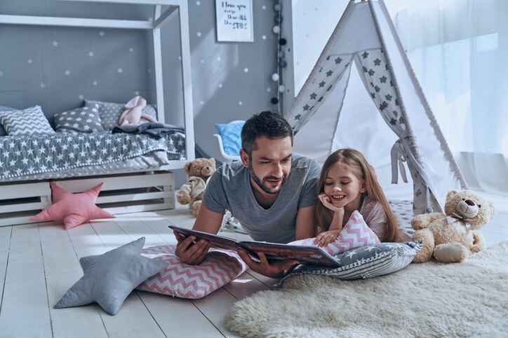 father and daughter reading a book inside home