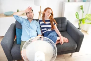 uncomfortable couple sitting on couch in front of fan