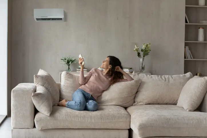 woman comfortable on couch controlling heat pump