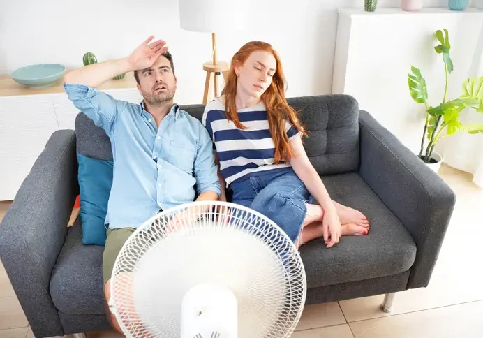 uncomfortable couple sitting on couch in front of fan