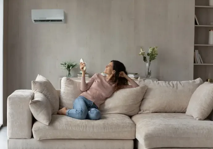 woman comfortable on couch controlling heat pump